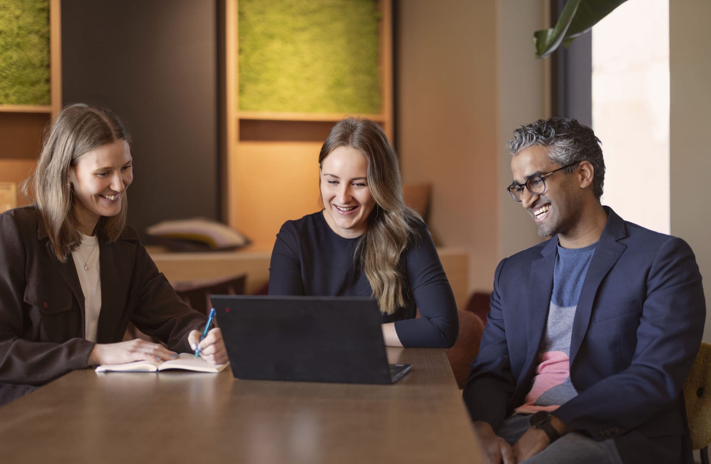 Three colleagues working together around a laptop.